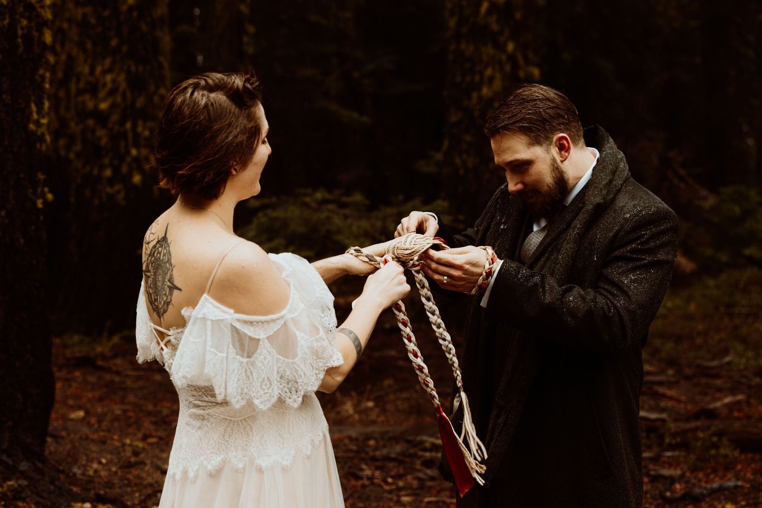 Bride and groom exchanging handfasting vows with a braided rope in an autumn forest.