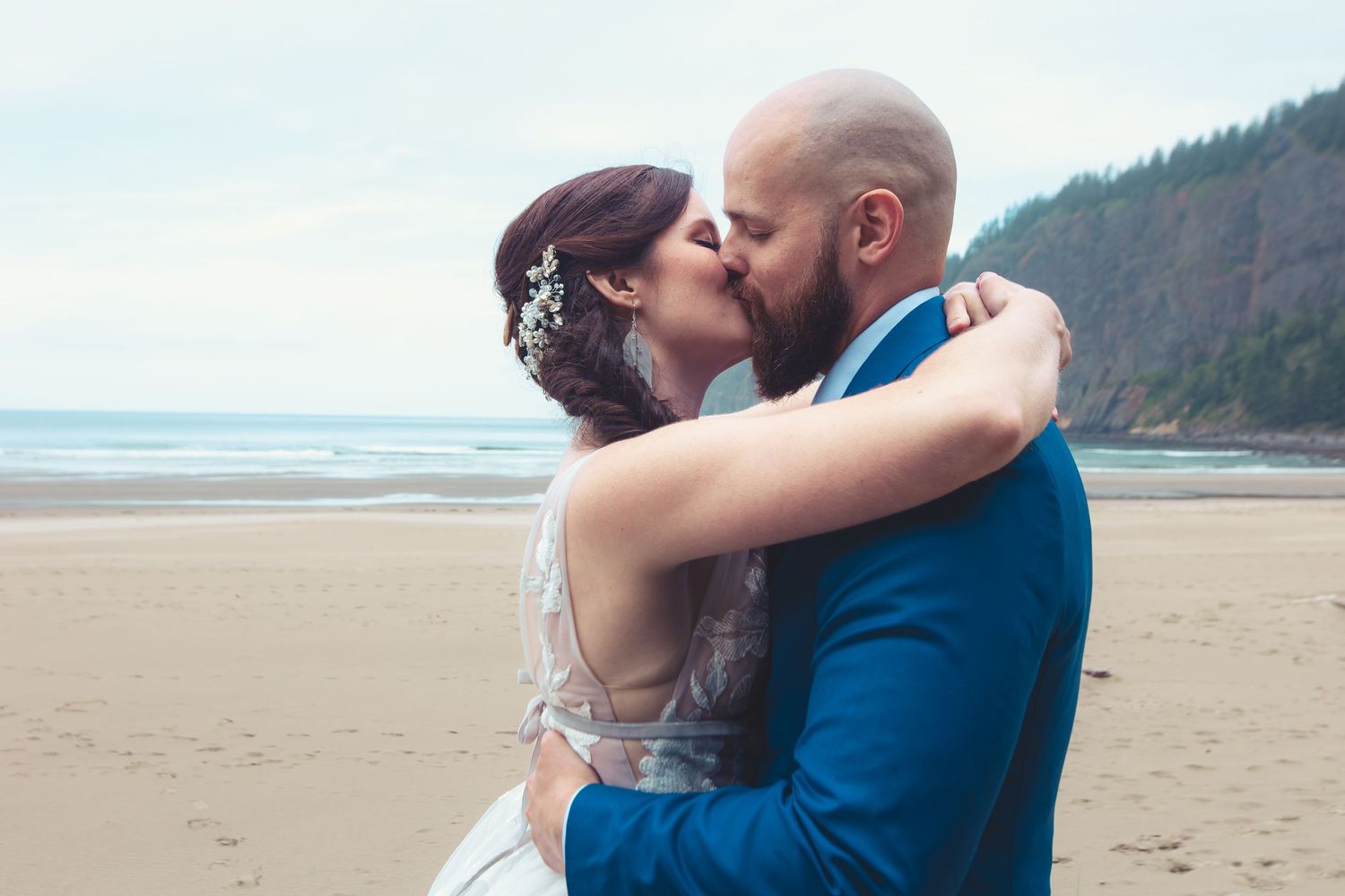 Bride and groom share a romantic kiss on the beach after their seaside wedding ceremony.