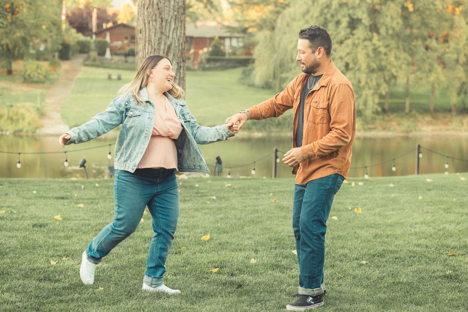 Smiling couple holding hands and dancing playfully in an autumn park.
