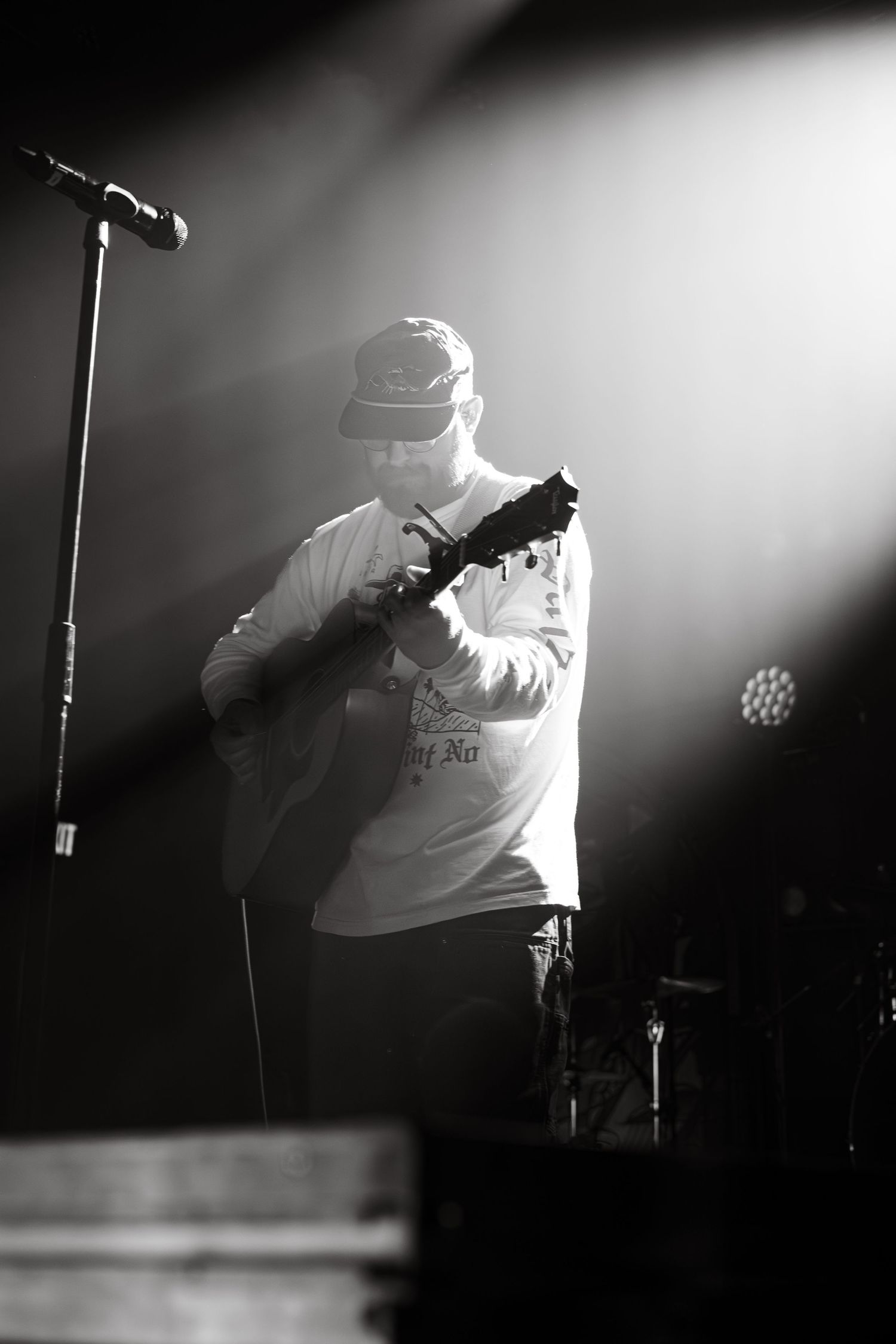 Black and white concert photo of guitarist performing on stage under dramatic spotlights.