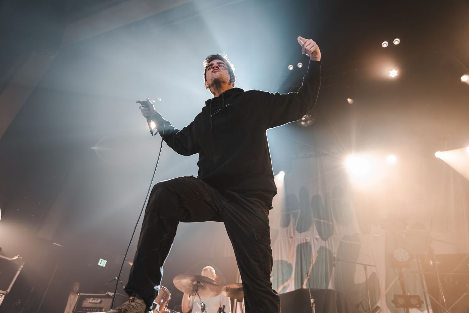 Low-angle view of male performer in black outfit striking dynamic pose on stage with bright concert lighting.