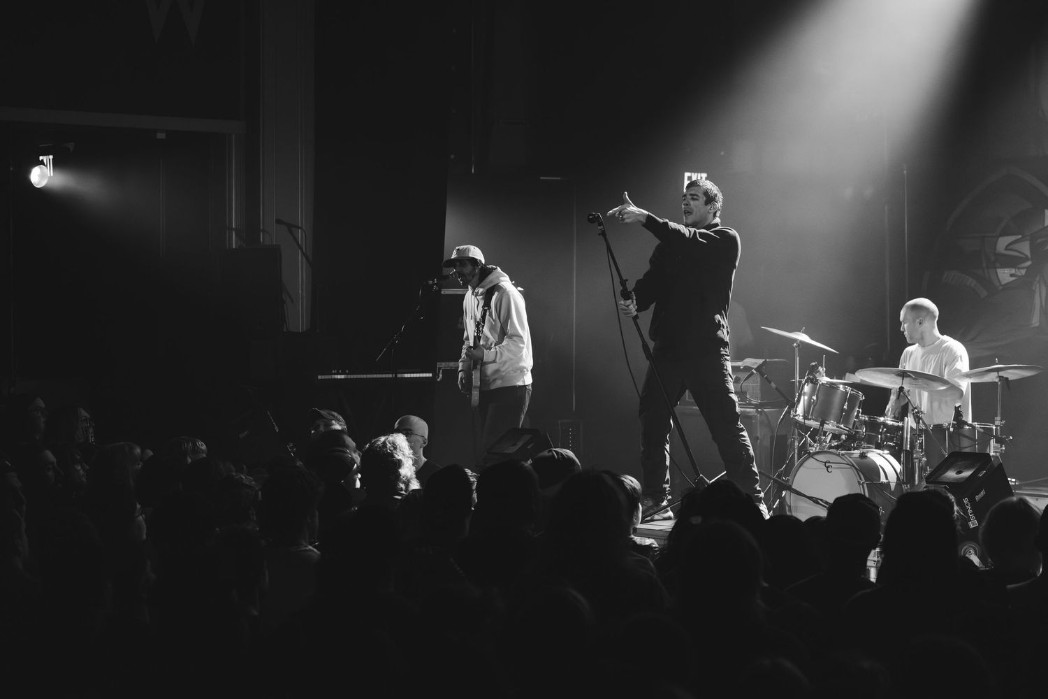 Black and white concert photo of band performing on stage with vocalist and guitarist under spotlight.