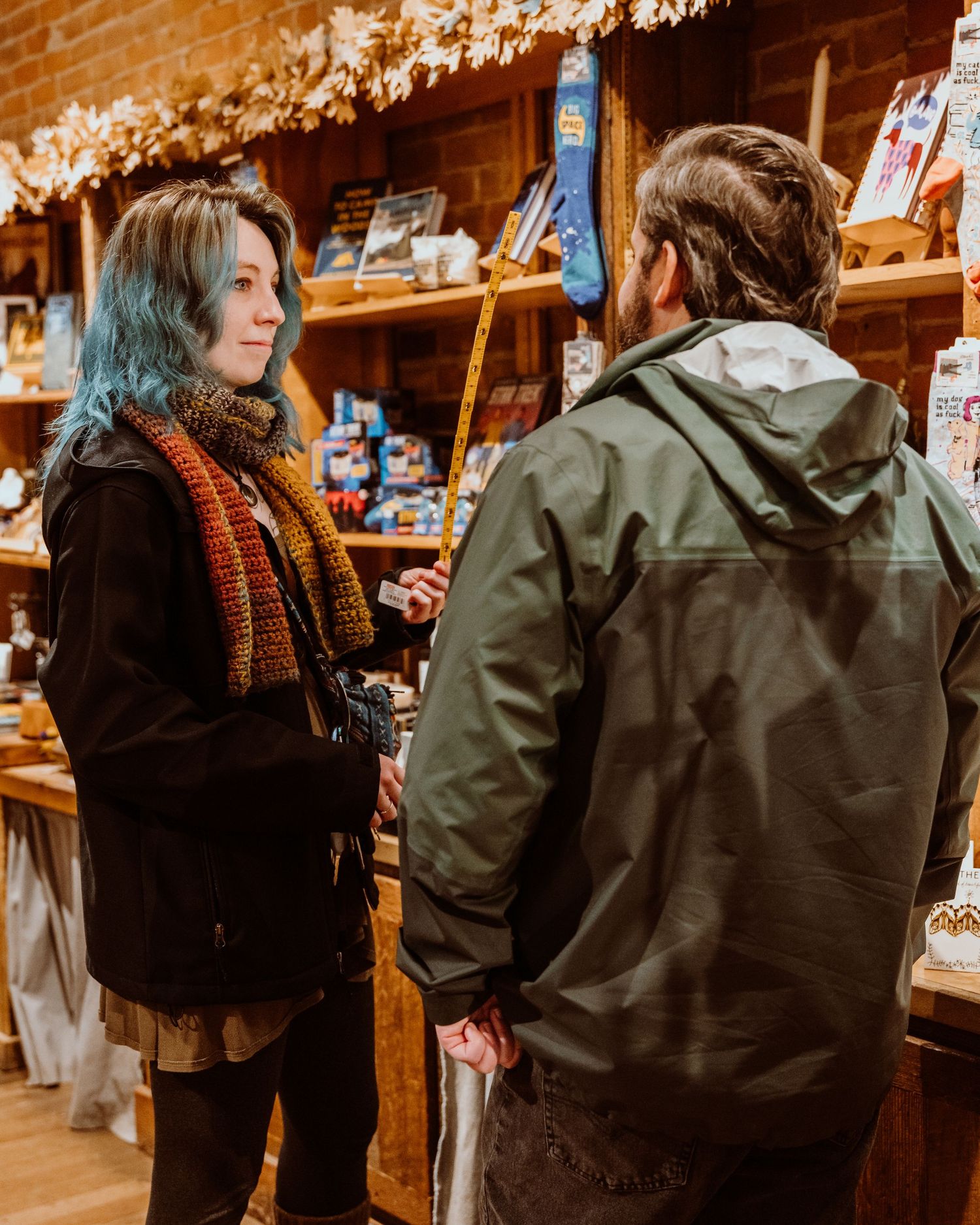 A woman with blue hair and colorful scarf talks with a man in a rustic shop.