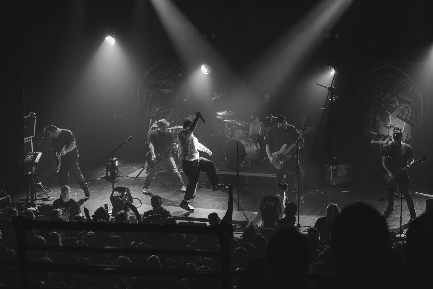 Black and white concert photo of energetic band performing on stage with dramatic lighting.