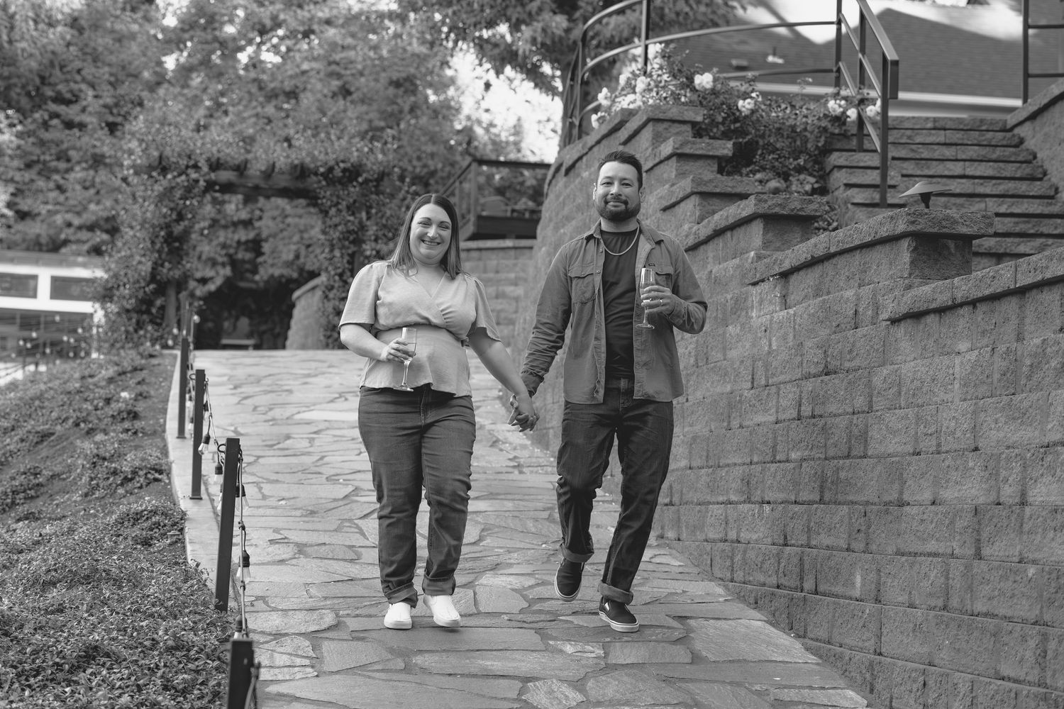 Black and white photo of a couple holding hands and laughing while walking along a stone path.