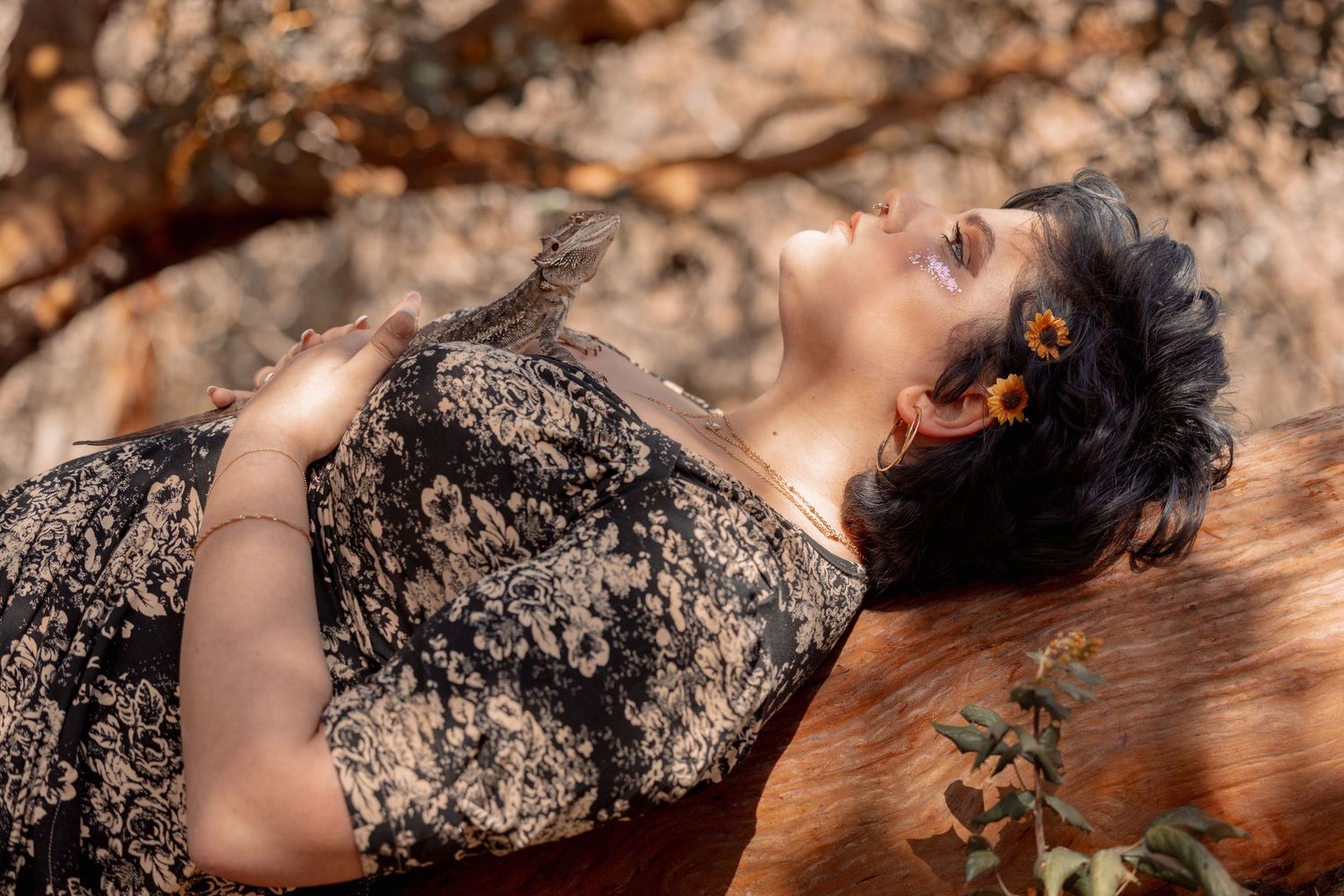 Woman with sunflower hair accessories reclines on a wooden surface outdoors in warm sunlight.