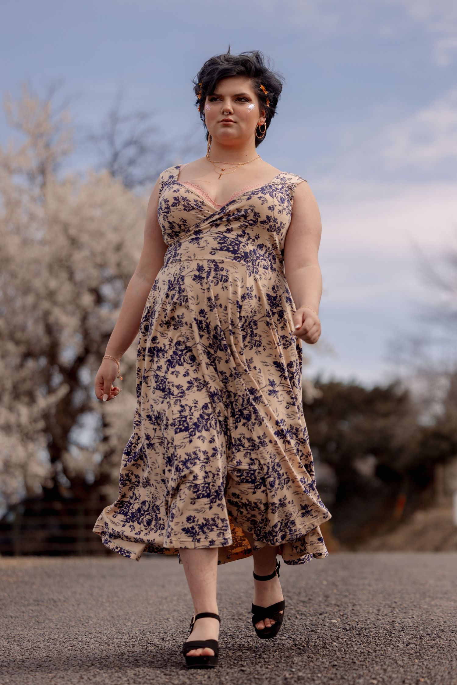 Woman in blue floral dress with ruffle hem walking on road near blooming spring trees.