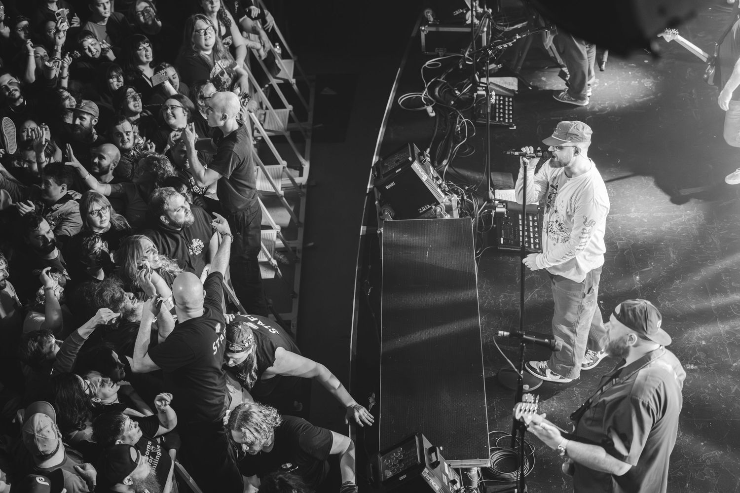 Black and white aerial view of a performer engaging with a packed concert crowd on stage.