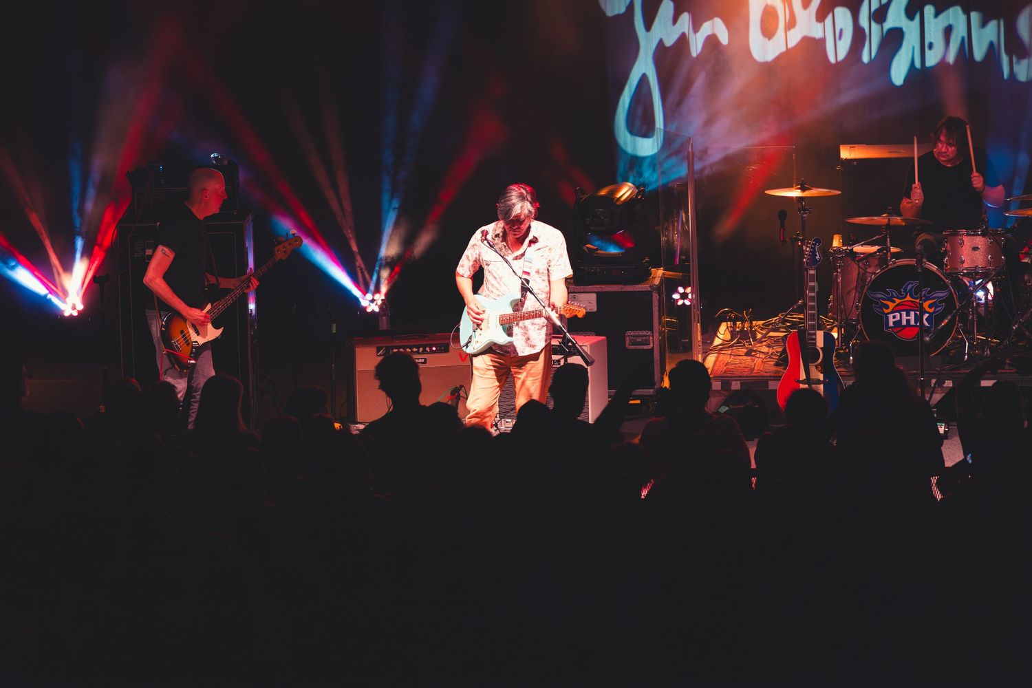 Band performing live on stage with dramatic blue and red lighting while audience watches from the floor.