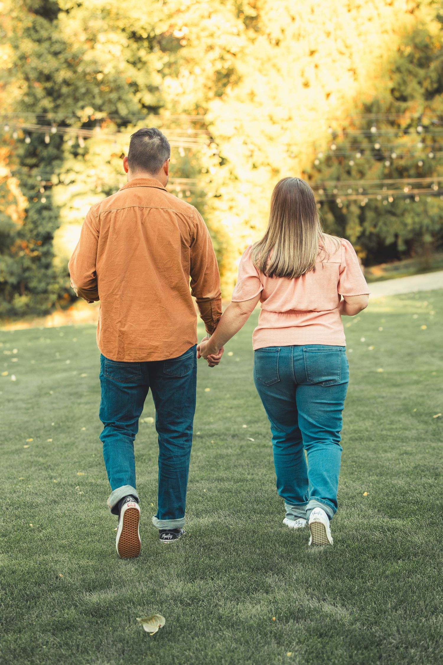 Couple walking hand in hand across a lush green lawn in a beautiful autumn garden setting.