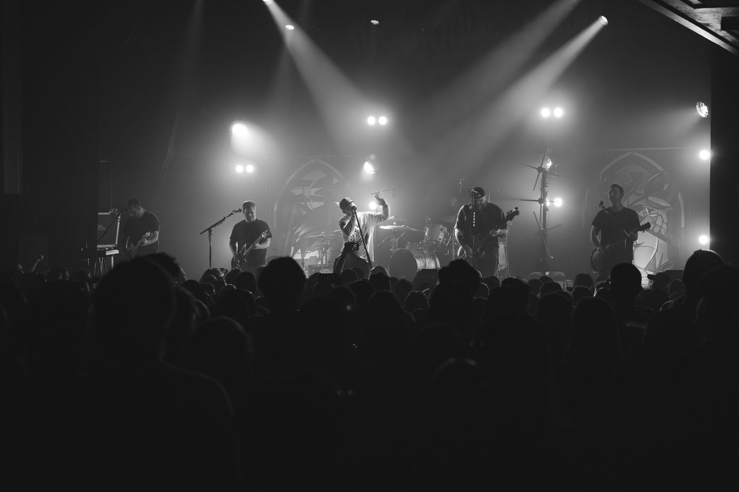 Black and white wide shot of a full band performing on a foggy, well-lit concert stage.