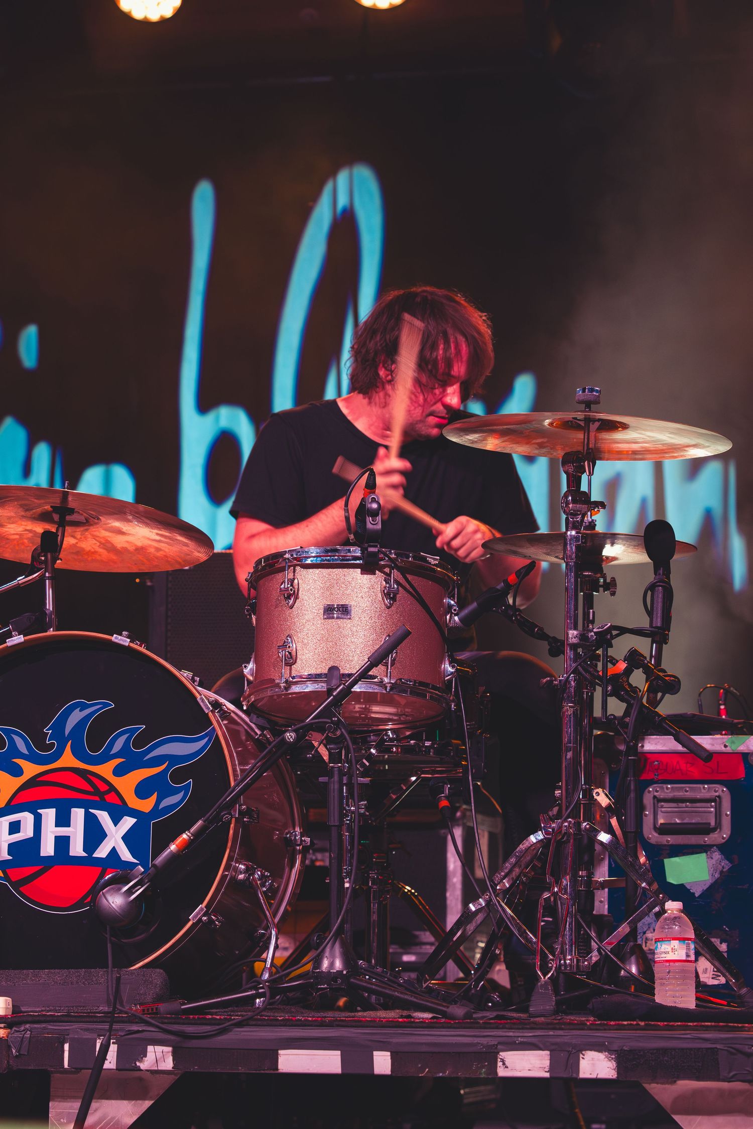 Energetic drummer plays a kit with a Phoenix Suns PHX logo bass drum on a lit stage.