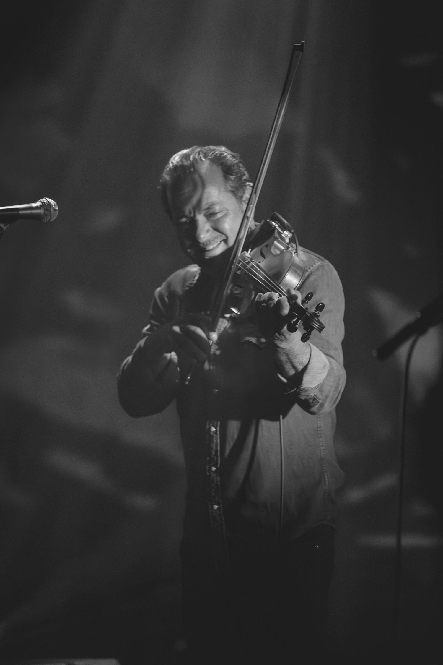 Black and white close-up of male violinist passionately playing violin under dramatic concert stage lighting.