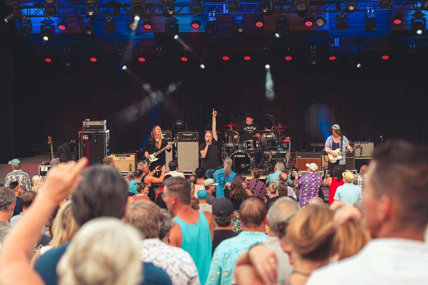 Rock band performing on a large outdoor stage to a lively festival audience.