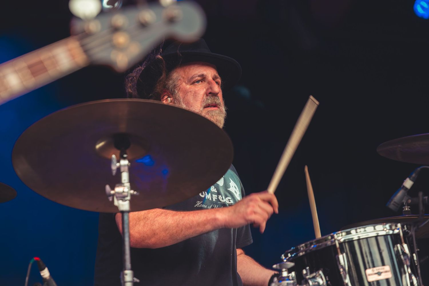 Bearded drummer playing cymbals passionately at a live rock music concert.