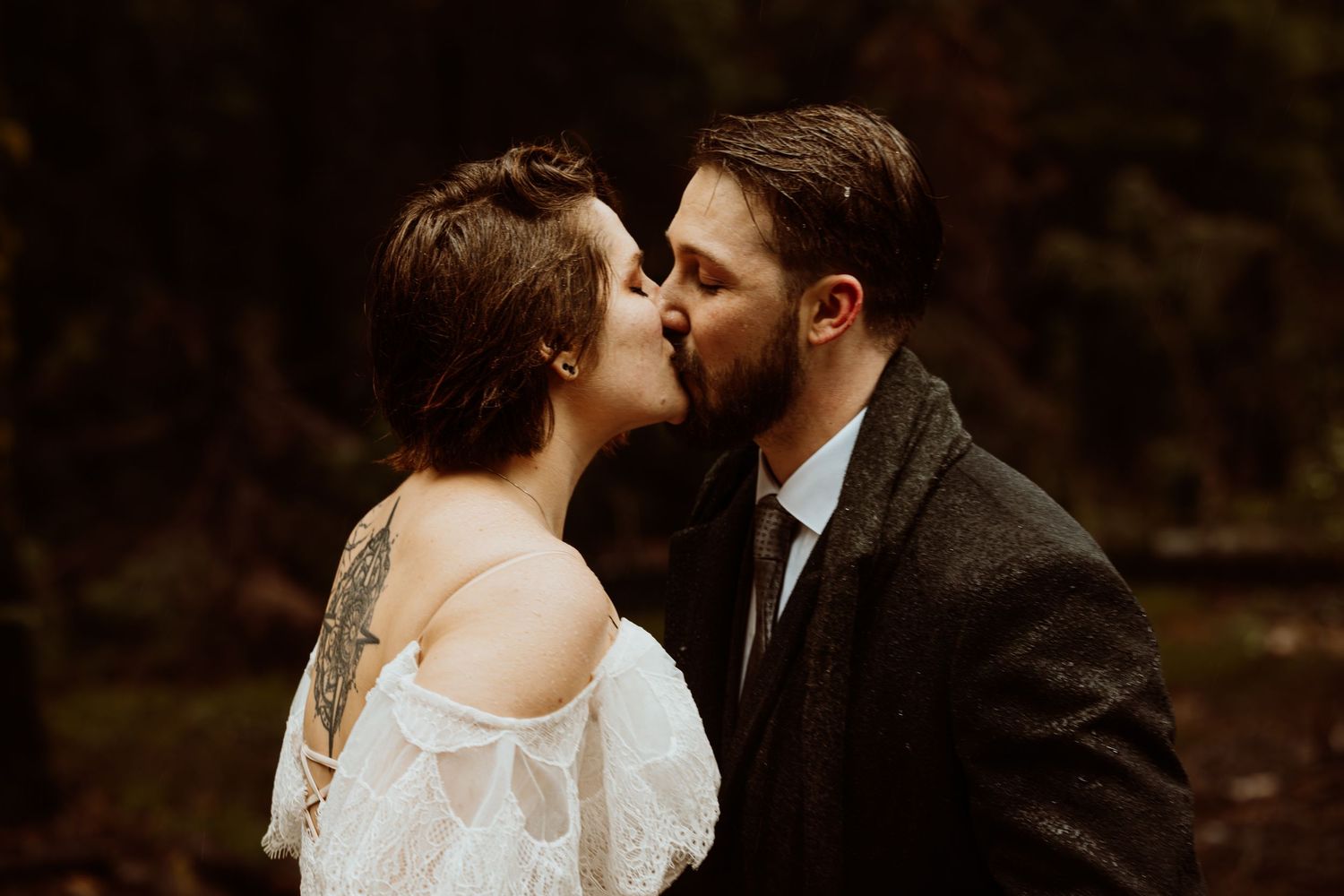 Couple sharing a romantic first kiss in a forest during their woodland wedding ceremony.