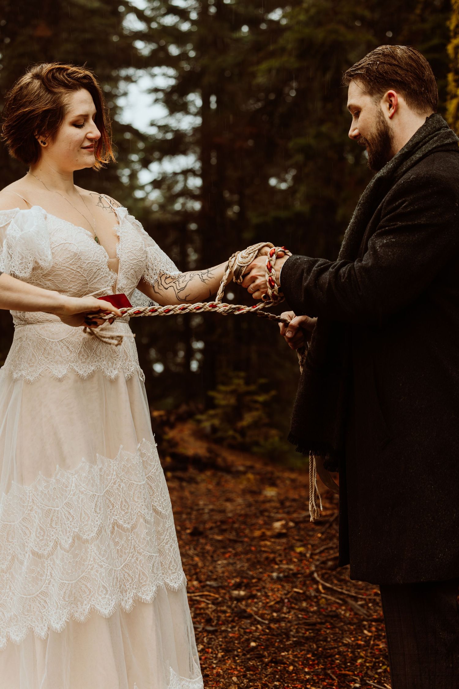 Bride and groom performing a handfasting ceremony in a forest, their hands bound with a braided rope.