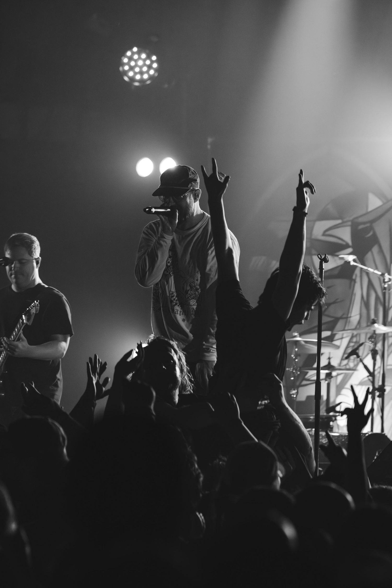 Black and white photo of vocalist performing in crowd with hands raised at a rock concert.