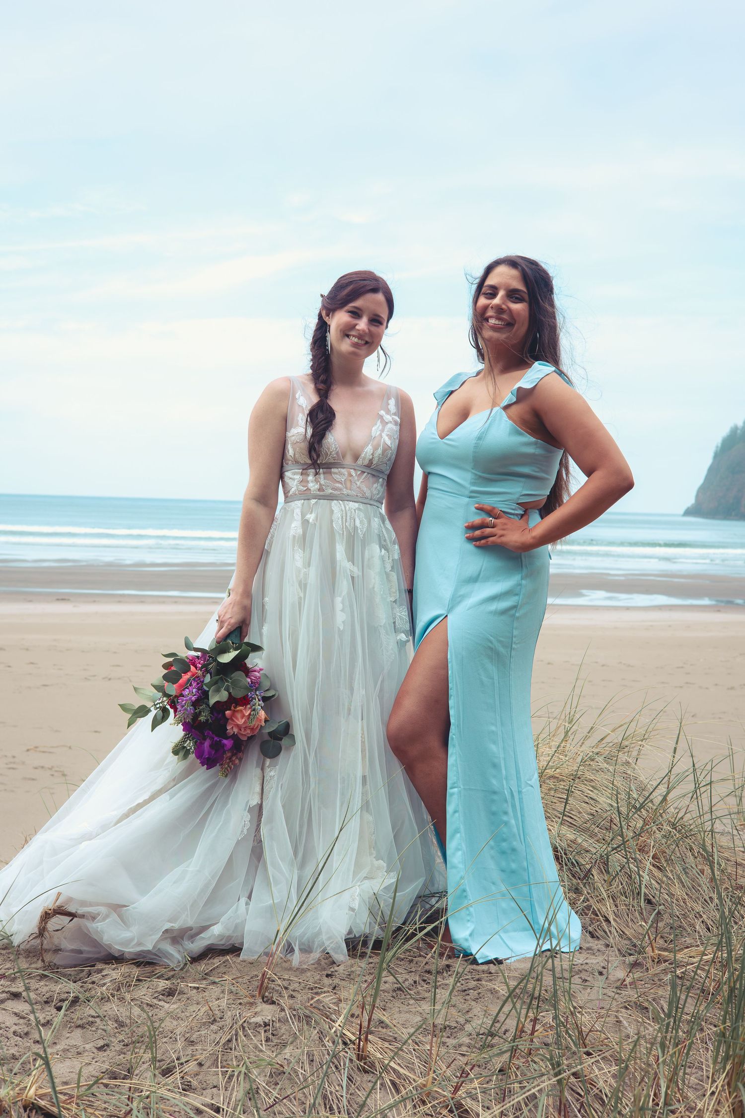Bride in white gown and bridesmaid in light blue dress pose on a beach wedding.