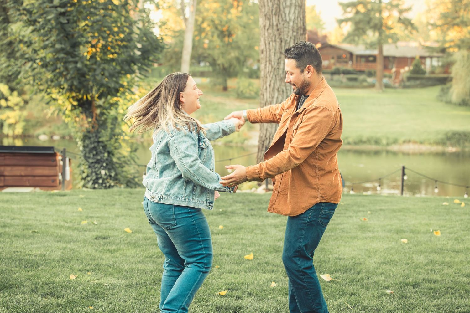 Happy couple spinning and dancing together on a green lawn by a pond.