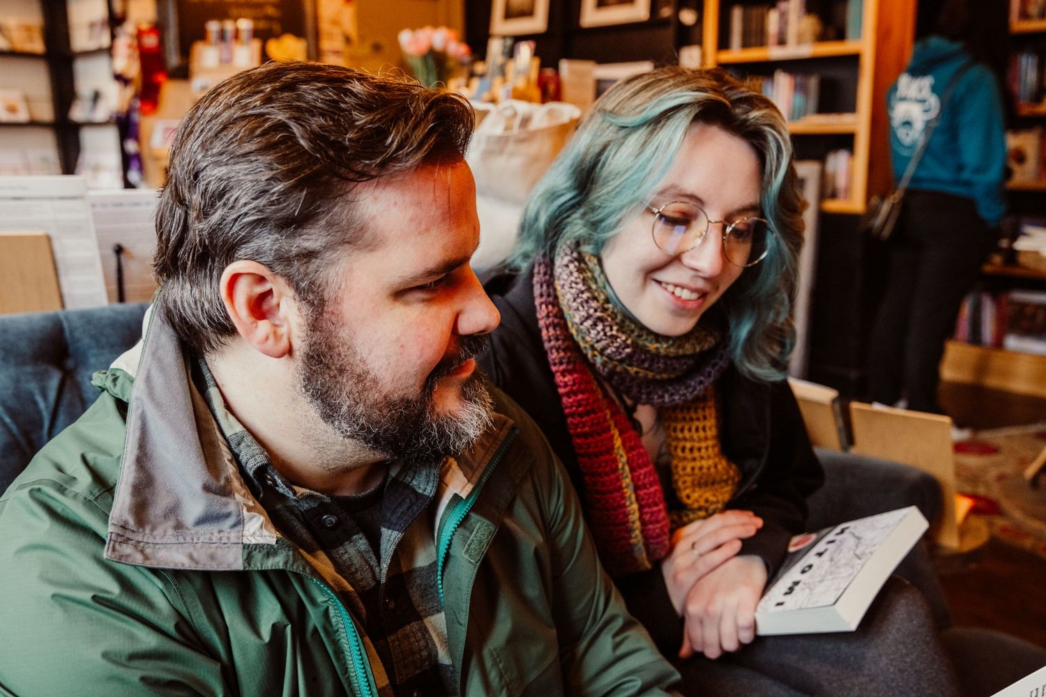 Smiling couple with blue-haired woman reading together in a cozy cafe.