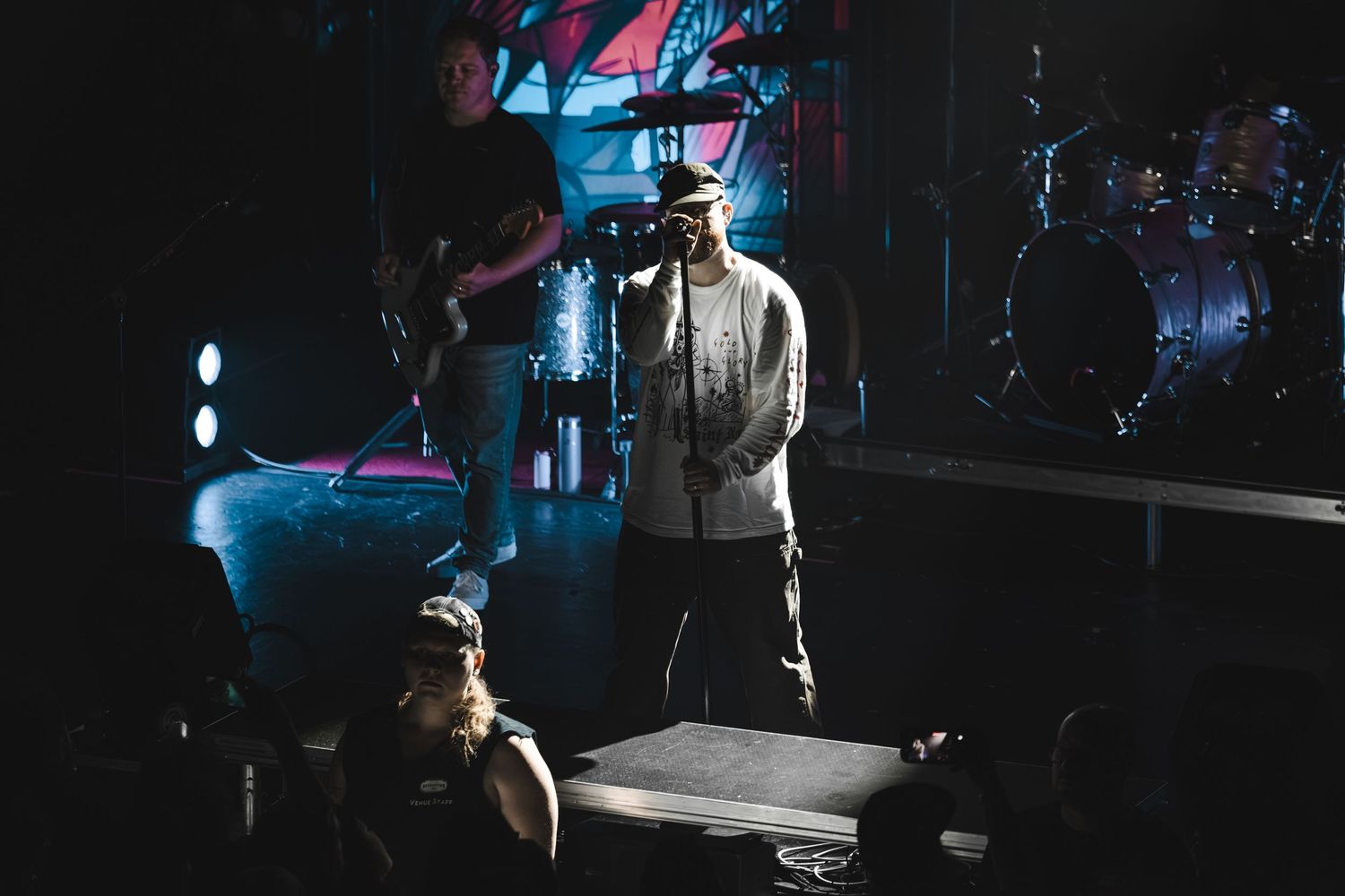 Musician performs on a darkly lit stage with dramatic blue and red lighting at a live show.