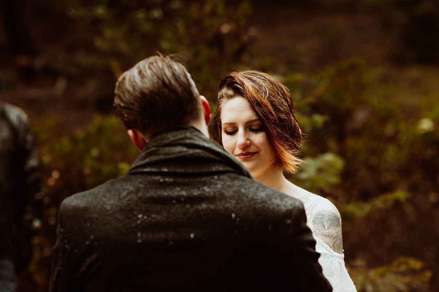 Close-up of bride with eyes closed leaning toward groom during emotional forest wedding ceremony.