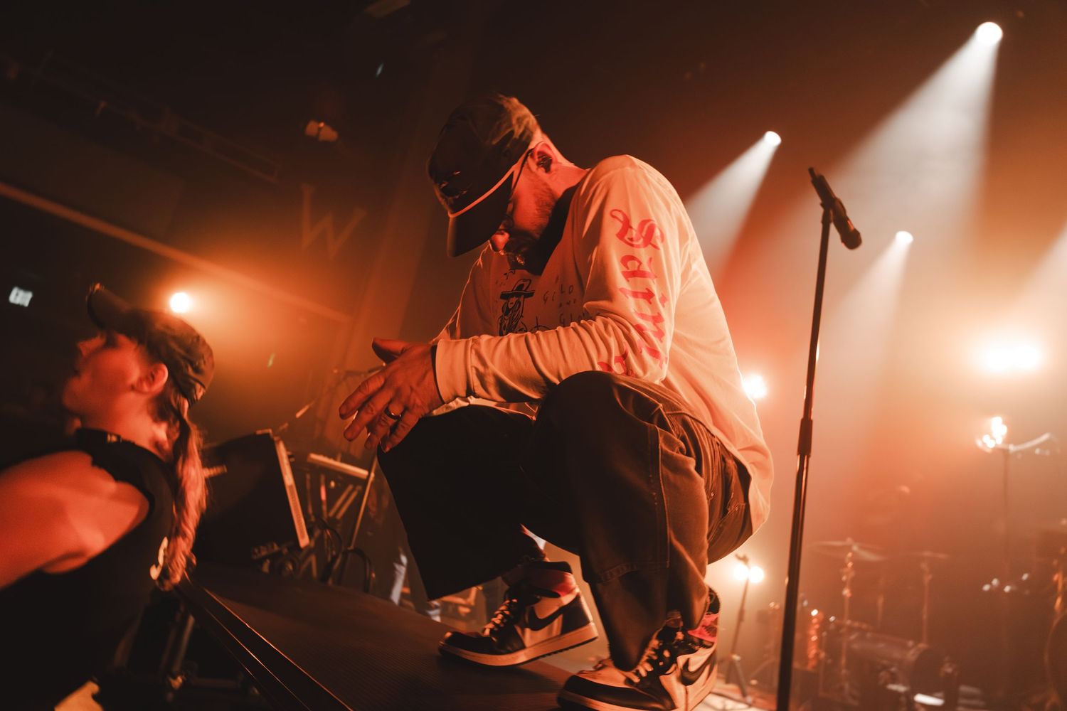 Concert performer crouching at stage edge engaging with crowd at live show.