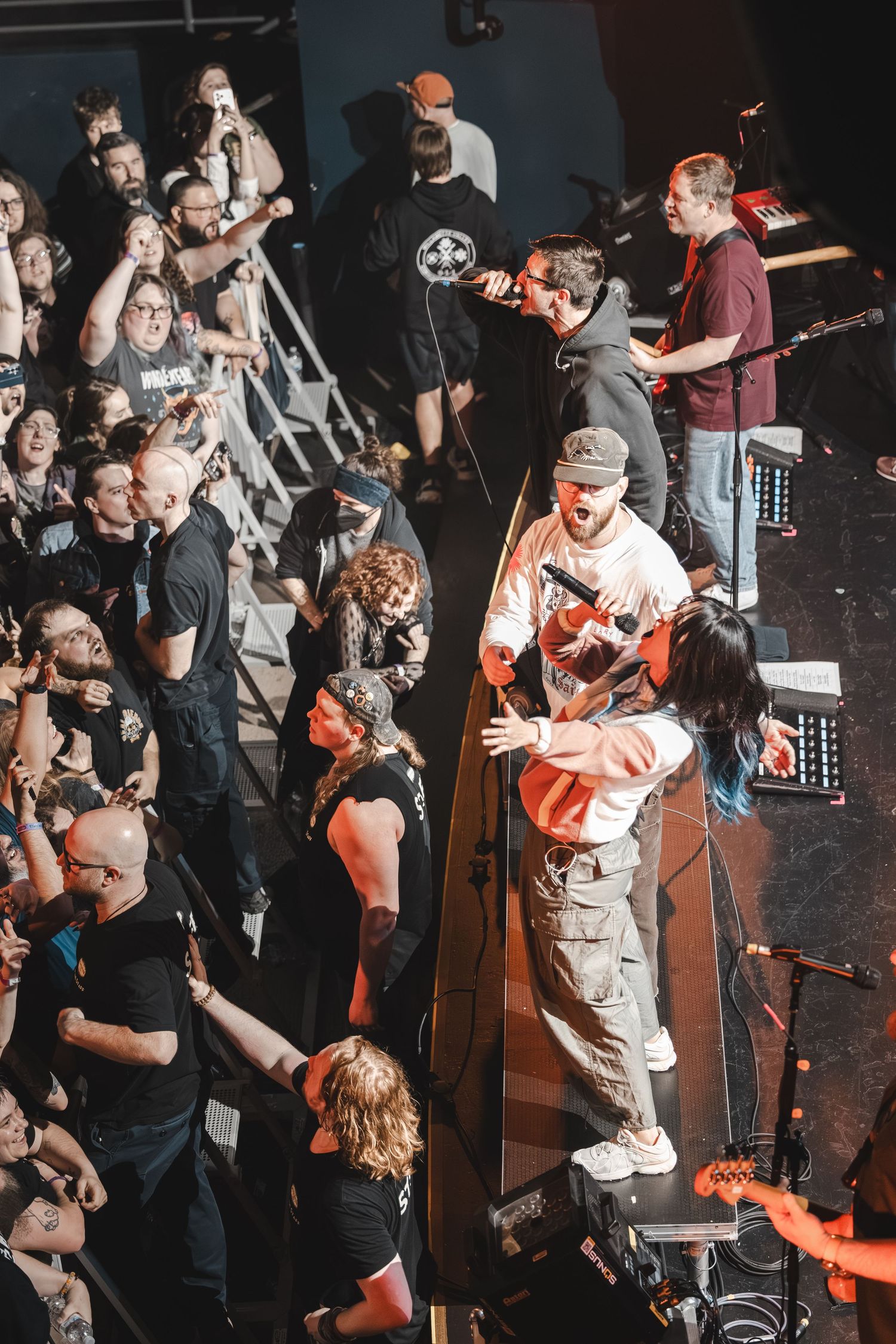 Aerial view of band members interacting with fans on the floor during a live concert.