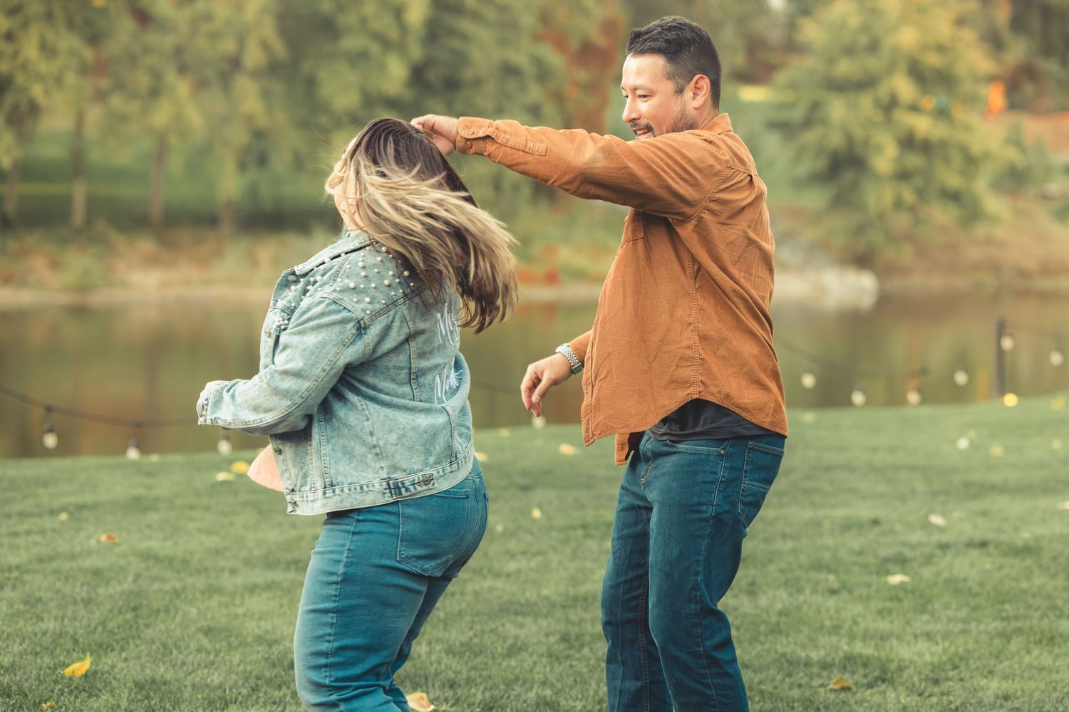 Couple dancing and spinning together near a scenic pond in autumn park.