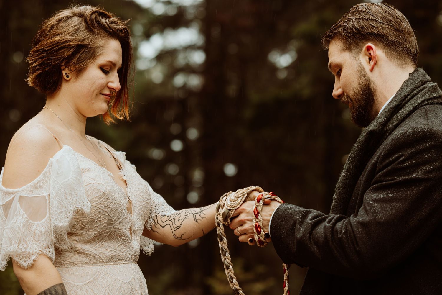 Couple performs handfasting ceremony with red cord binding their hands in intimate outdoor wedding.