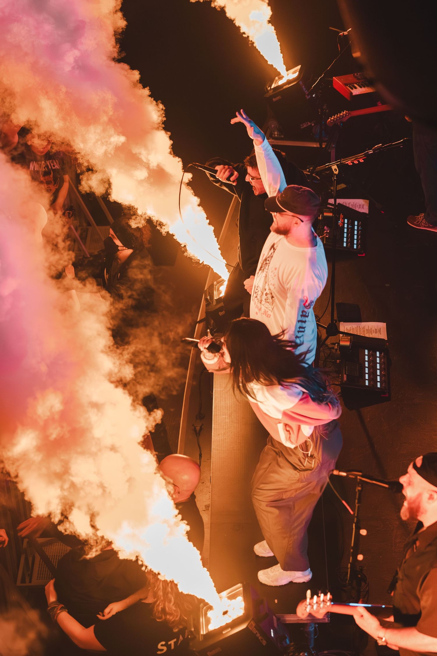 Performer on stage with pyrotechnic flames and smoke during an energetic live concert.