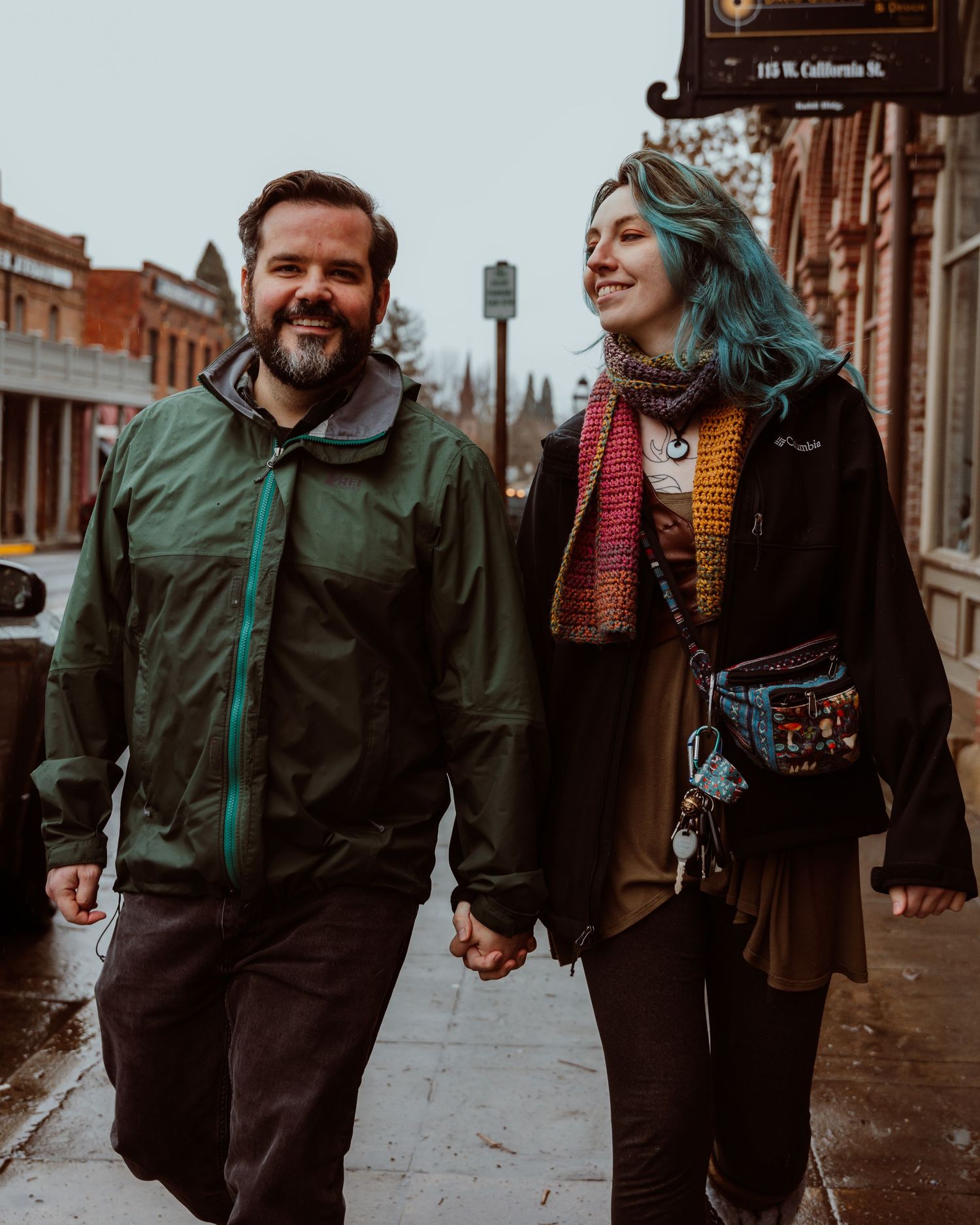 A happy couple holding hands and walking along a rainy historic downtown street.