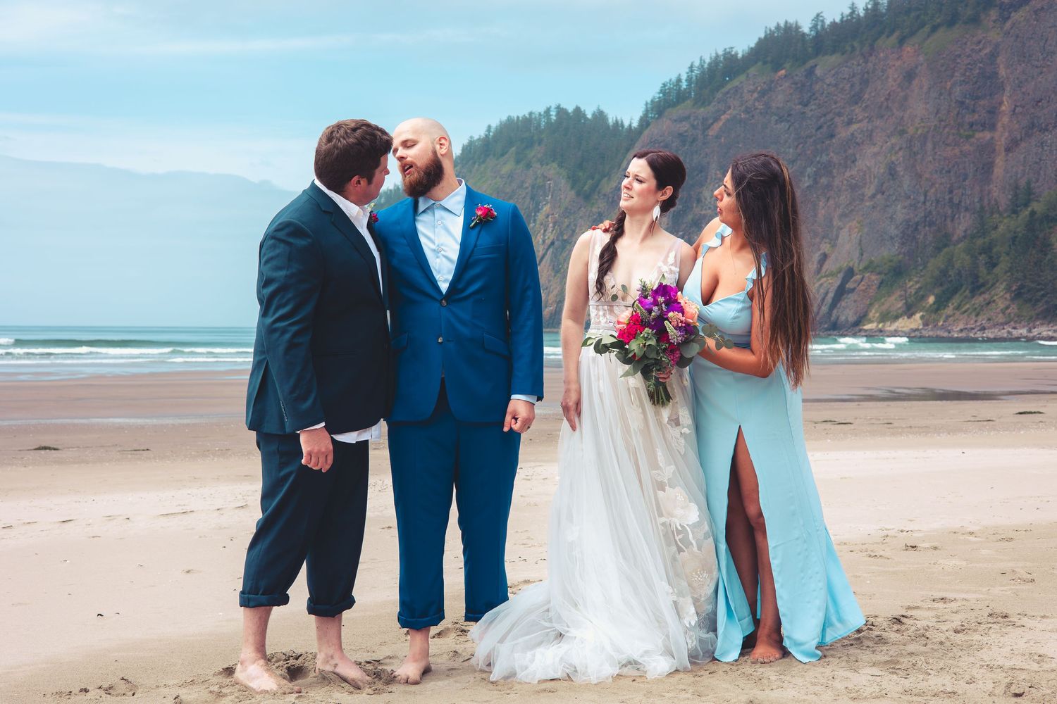 Bride and groom with wedding party posing on a scenic beach with towering rocky cliffs.