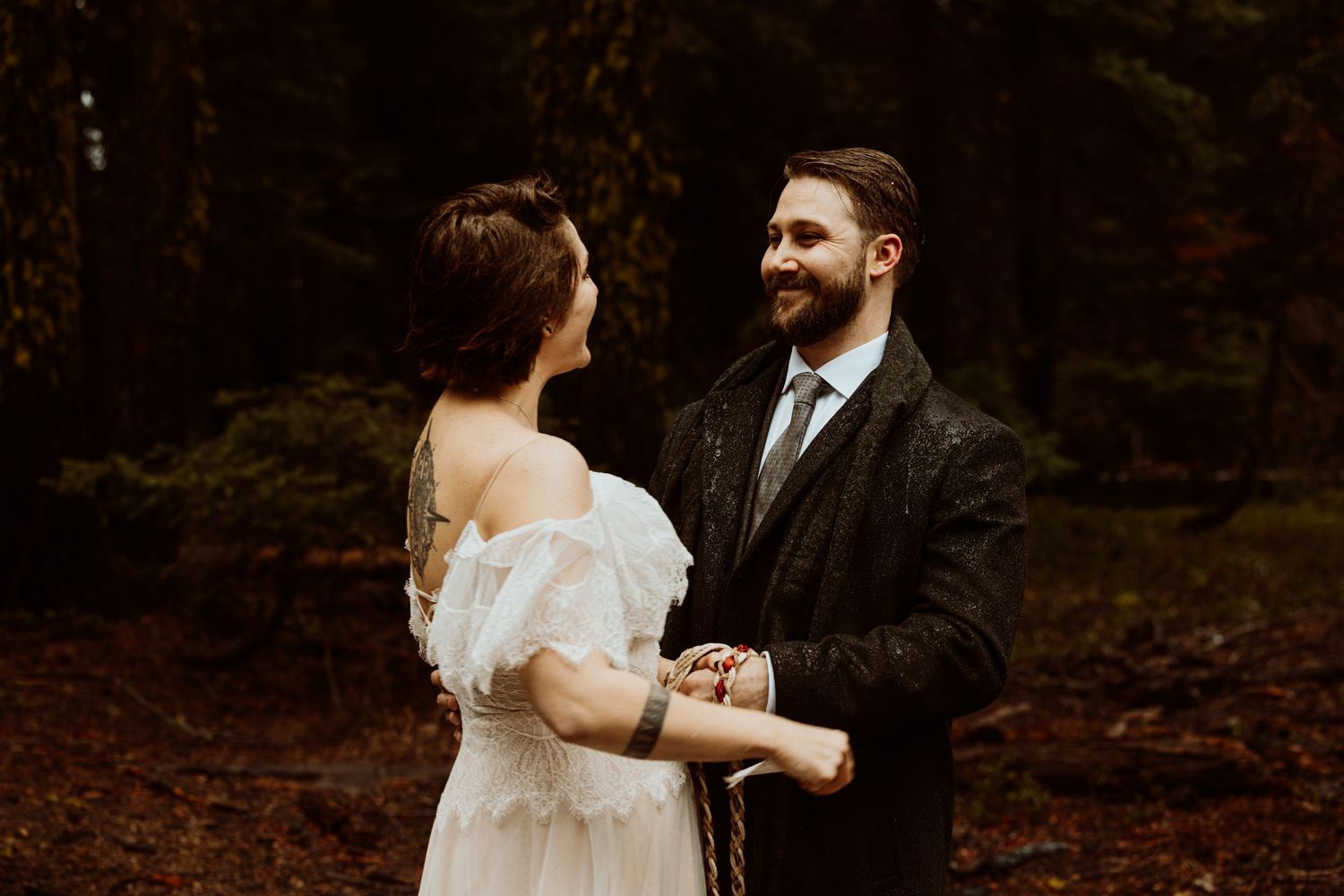 Smiling groom holds bride's hands during an intimate outdoor forest wedding ceremony.