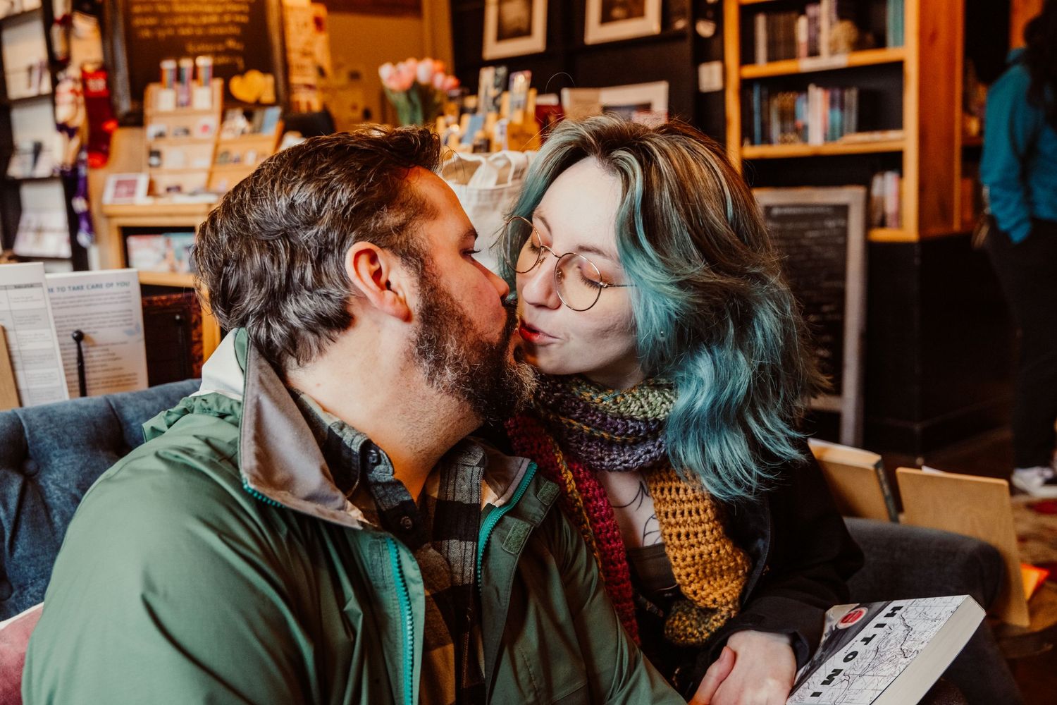 Couple sharing a romantic kiss in a warm, book-filled cafe.