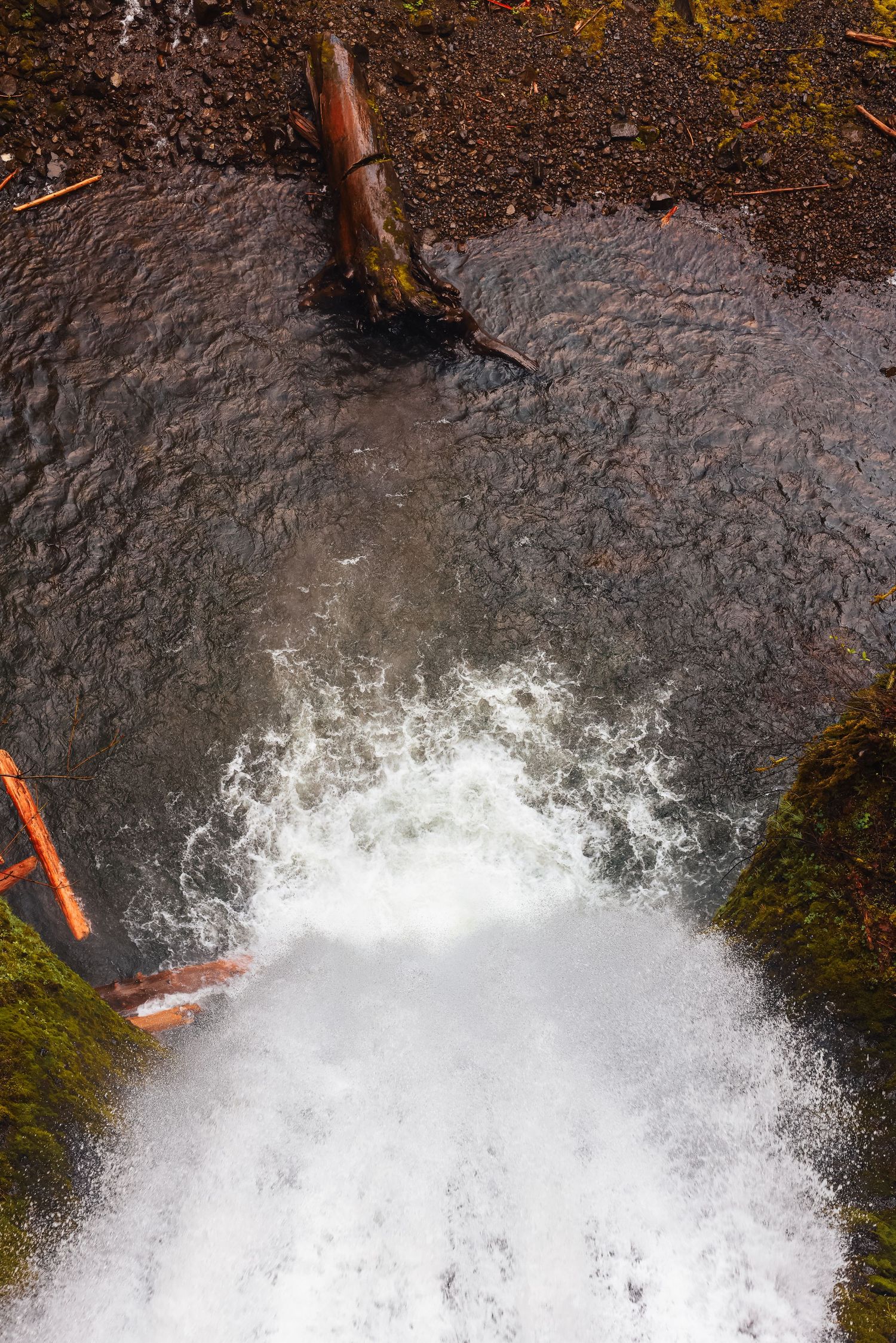 Rushing white water splashes at the base of a waterfall over mossy rocks.