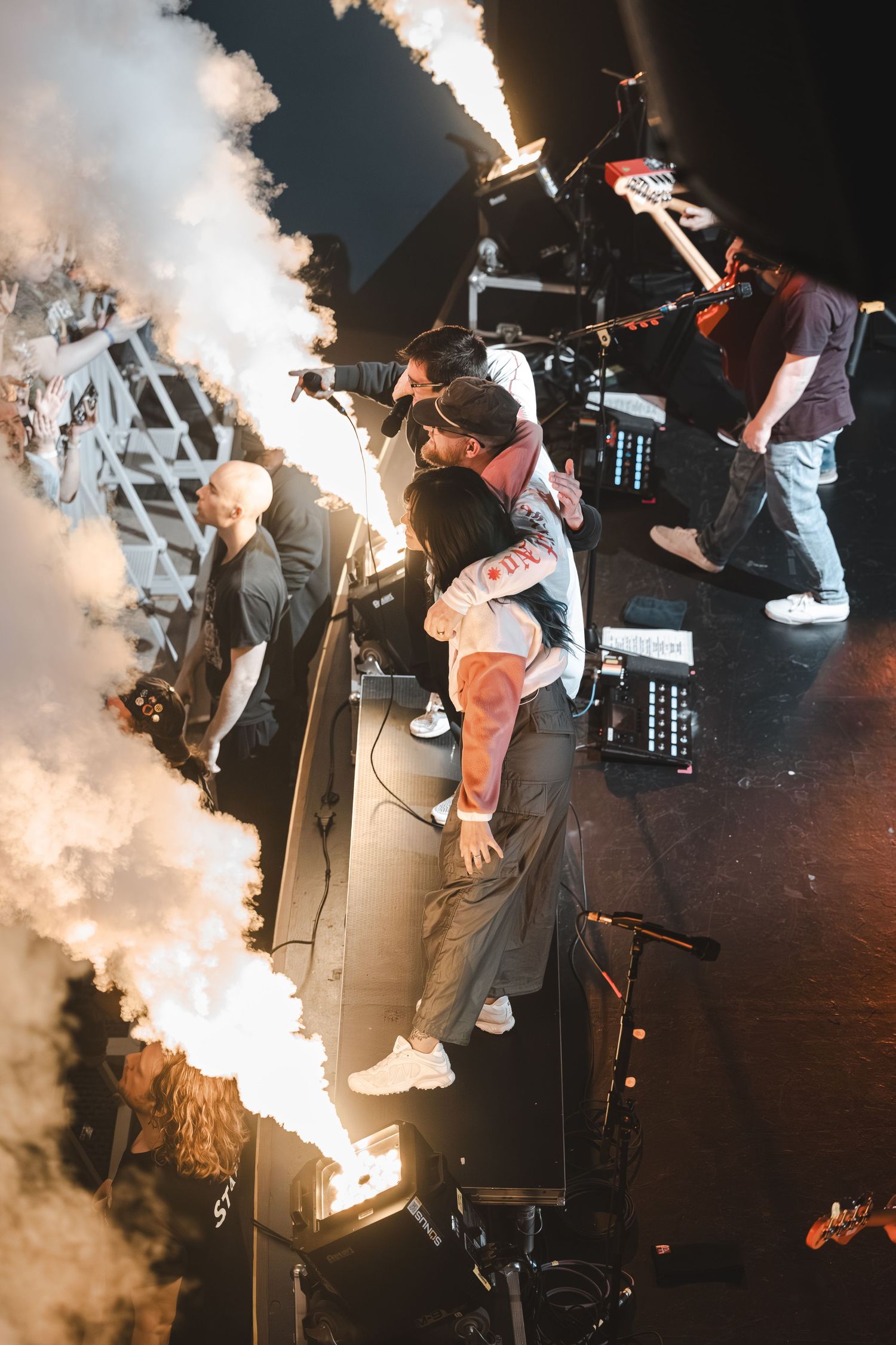 Band members on stage surrounded by fire and smoke effects during a live performance.