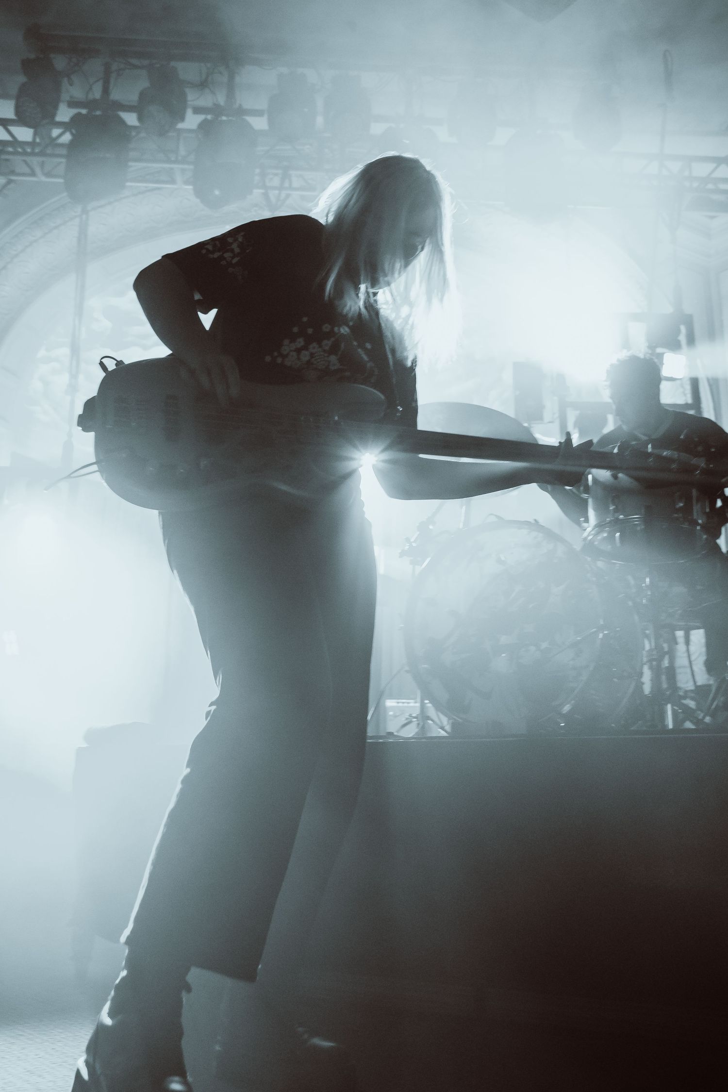 Silhouetted guitarist performing on a foggy concert stage with dramatic blue-white lighting.