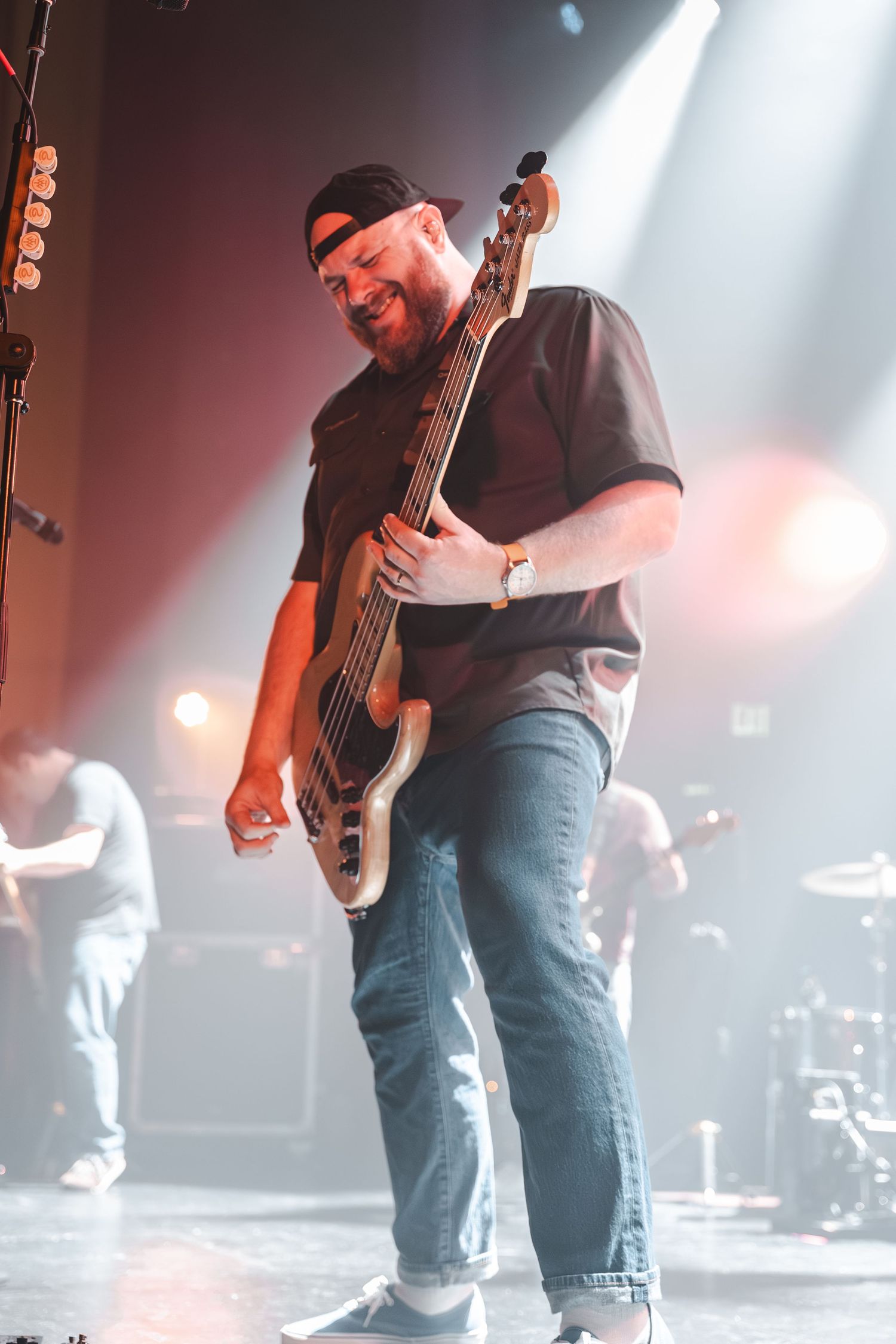 Smiling bassist playing five-string bass guitar on stage at a live concert.