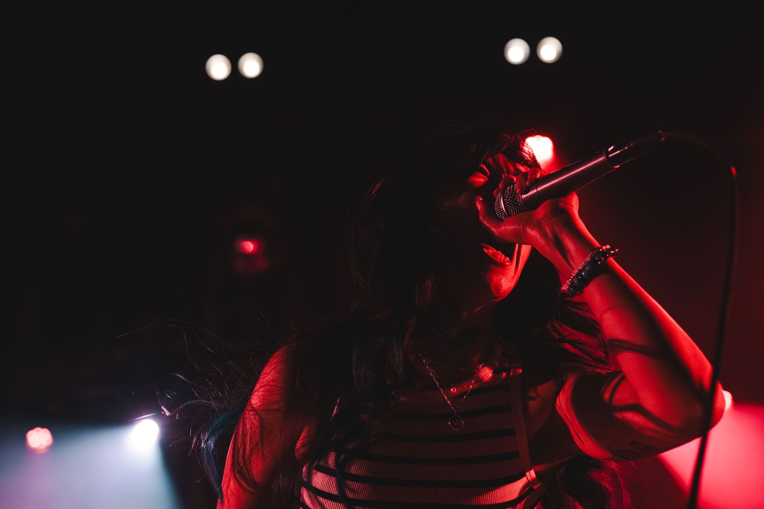 Close-up of female singer holding microphone to her face under dramatic red stage lighting.