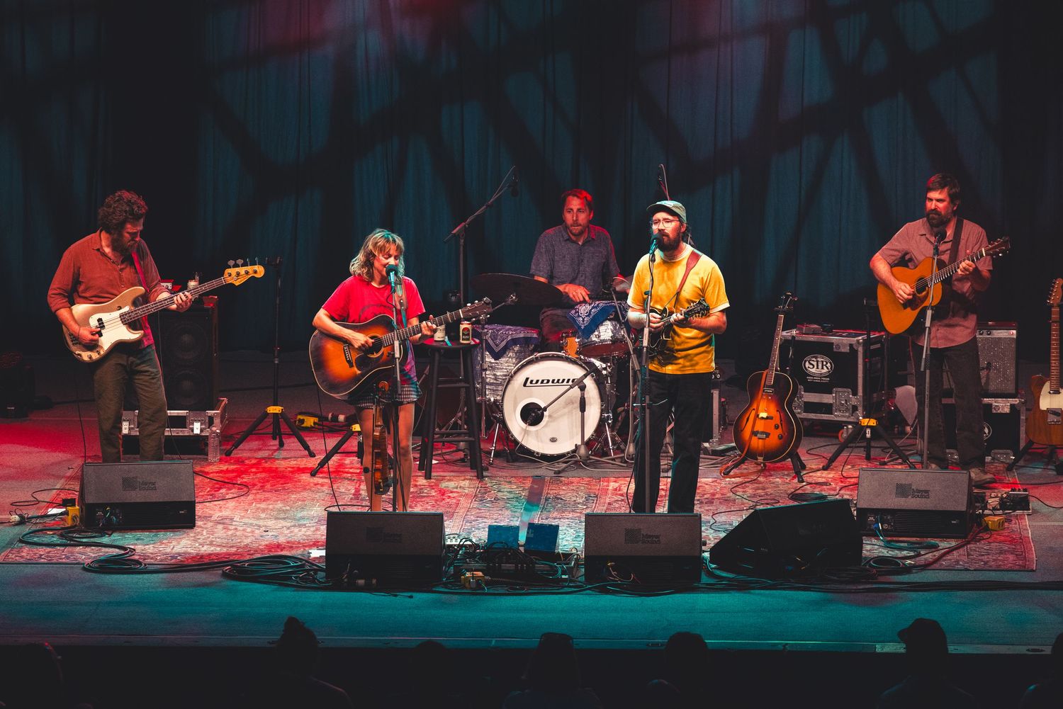 Five-piece indie folk band performing on a dramatic red and blue lit indoor concert stage.