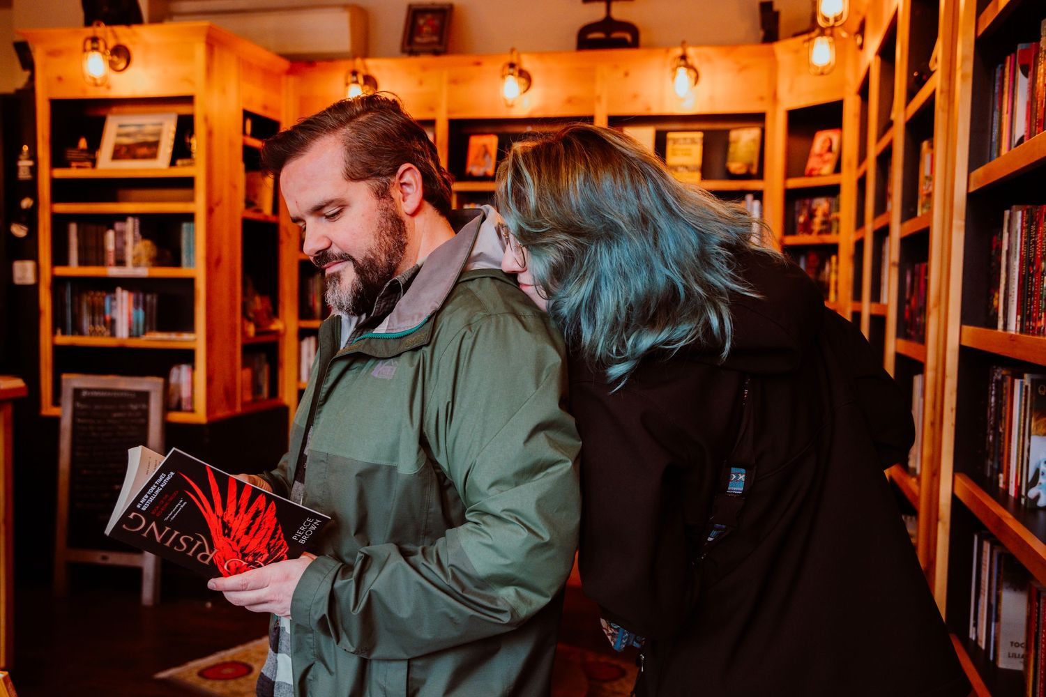 Couple sharing a laugh over a book in a warmly lit wooden bookstore.