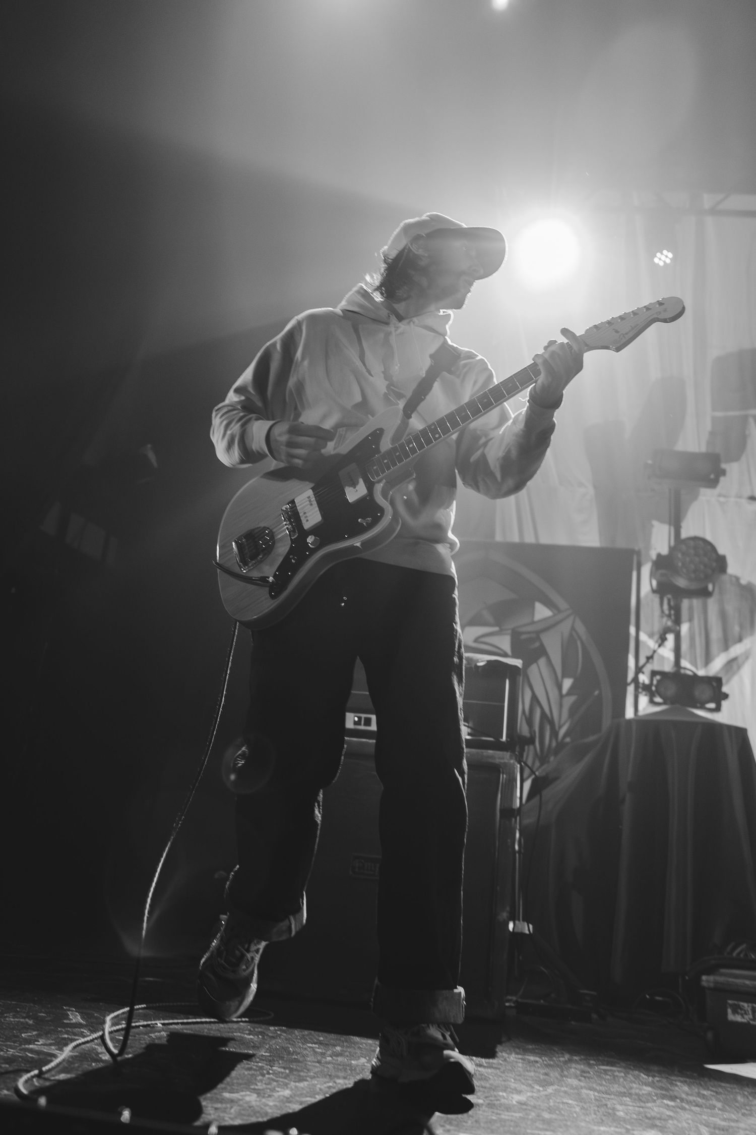 Black and white shot of a guitarist playing electric guitar on stage under bright concert spotlights.