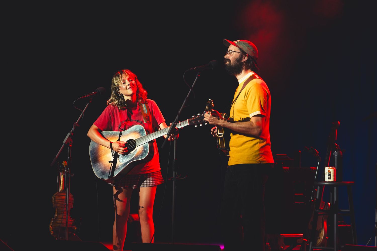 A woman and man perform folk music on acoustic guitars at a dimly lit concert stage.