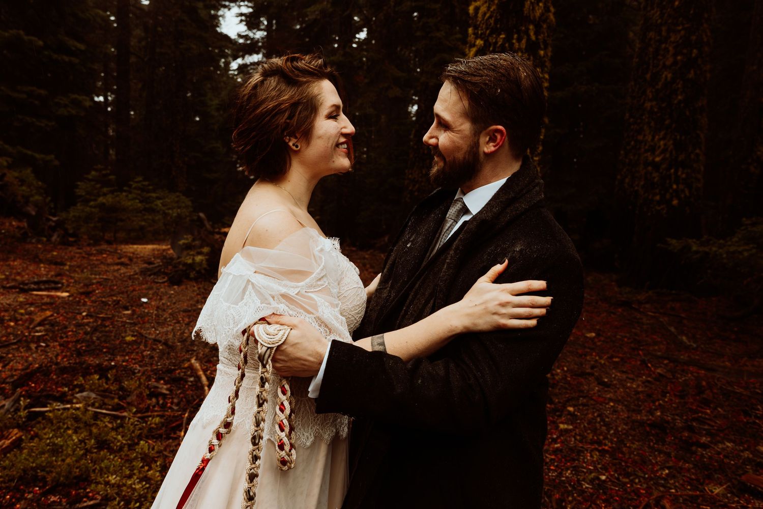 Bride and groom gazing at each other tenderly with handfasting cord in an autumn forest.