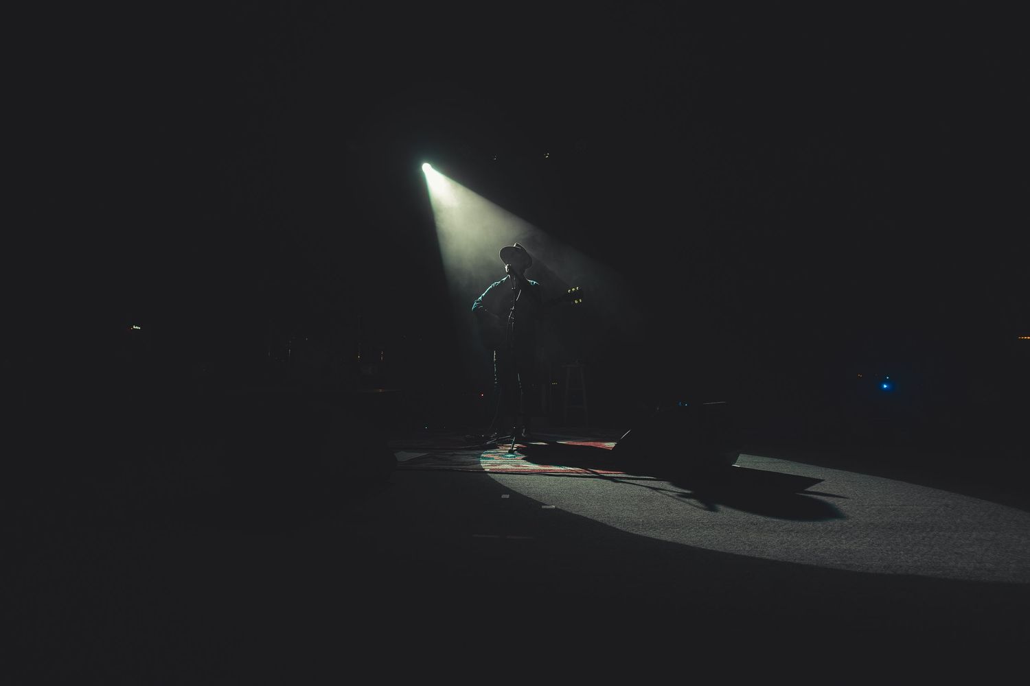 Lone musician performs under single spotlight on darkened concert stage.