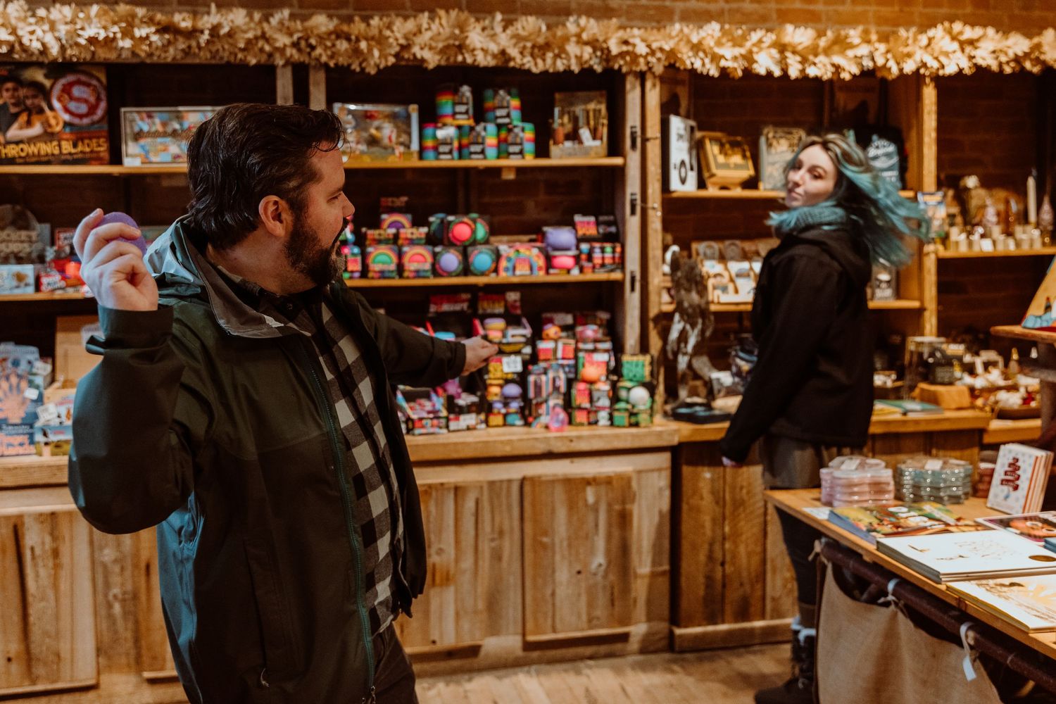 Bearded man and blue-haired woman browsing colorful items in a rustic store.