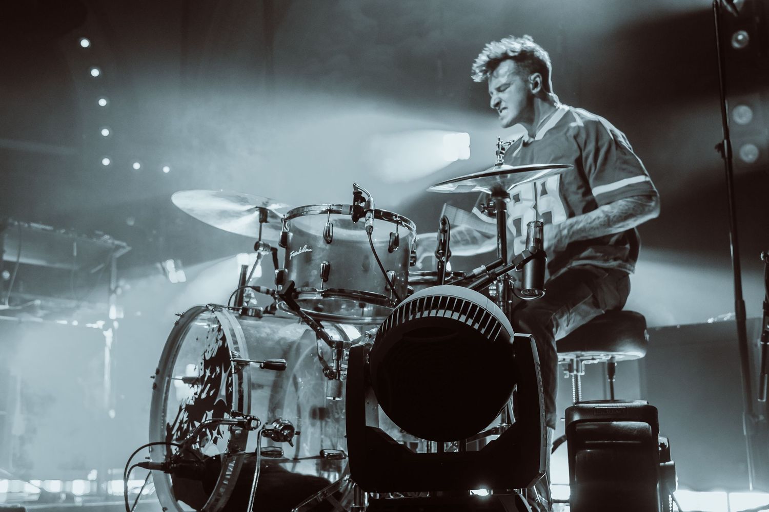 Male drummer performing on stage in black and white with dramatic fog and lighting.