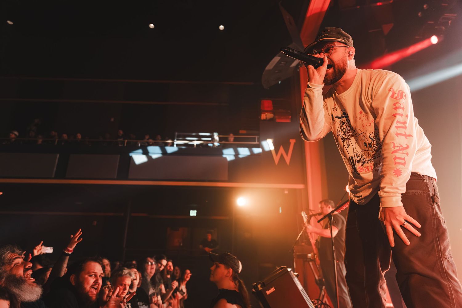 Male rapper performing on stage with microphone at a live concert venue.